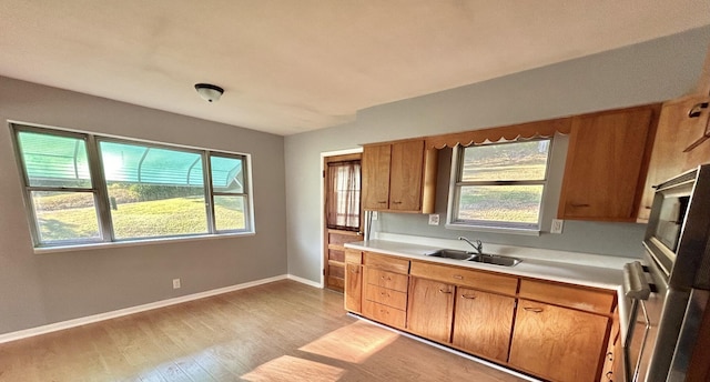 kitchen featuring a sink, baseboards, light countertops, light wood finished floors, and brown cabinetry