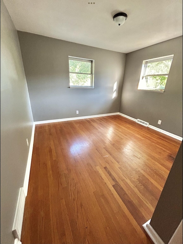 empty room with a wealth of natural light, baseboards, and wood finished floors