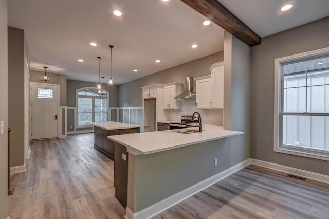 kitchen with a sink, visible vents, white cabinets, light countertops, and wall chimney range hood