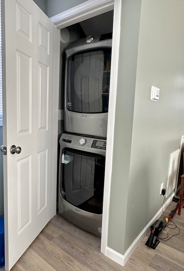 laundry area with stacked washer and clothes dryer and light wood-type flooring