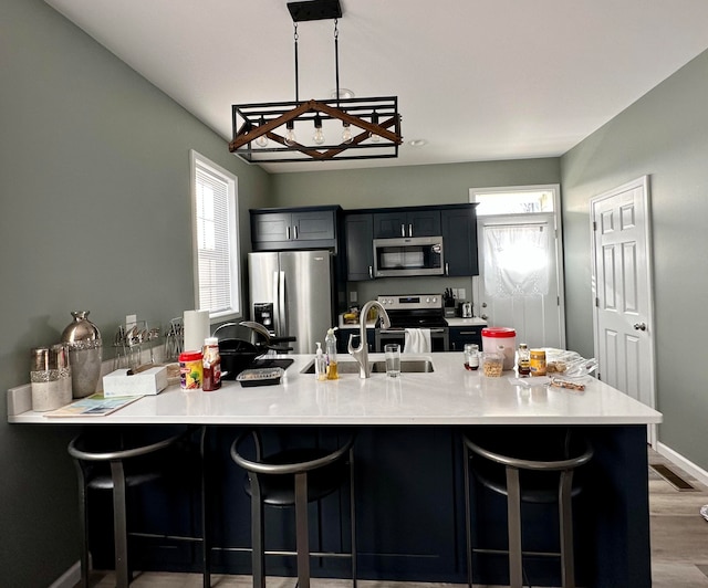 kitchen featuring hardwood / wood-style flooring, appliances with stainless steel finishes, a notable chandelier, pendant lighting, and a kitchen bar