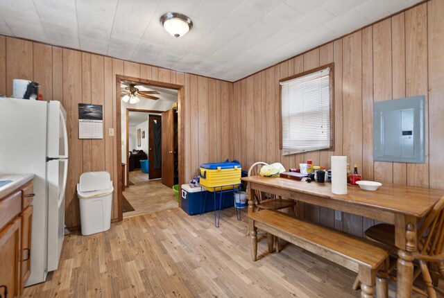 dining area featuring wood walls, light hardwood / wood-style flooring, electric panel, and ceiling fan