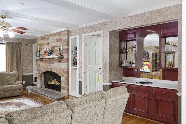 living room featuring ceiling fan, crown molding, light wood-type flooring, and a fireplace