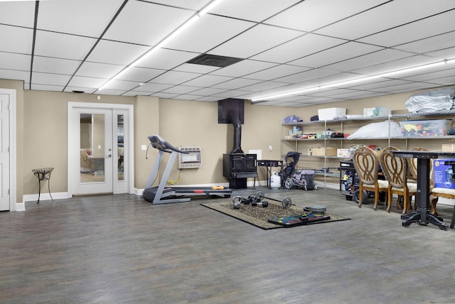 exercise room with french doors, a wood stove, a paneled ceiling, and wood-type flooring