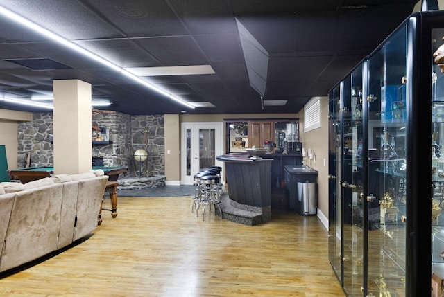 interior space with light wood-type flooring, a paneled ceiling, a stone fireplace, pool table, and bar