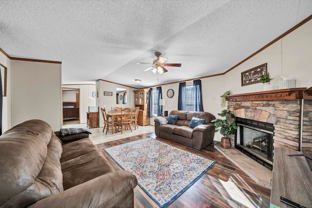 living room featuring ceiling fan, a textured ceiling, crown molding, and a stone fireplace