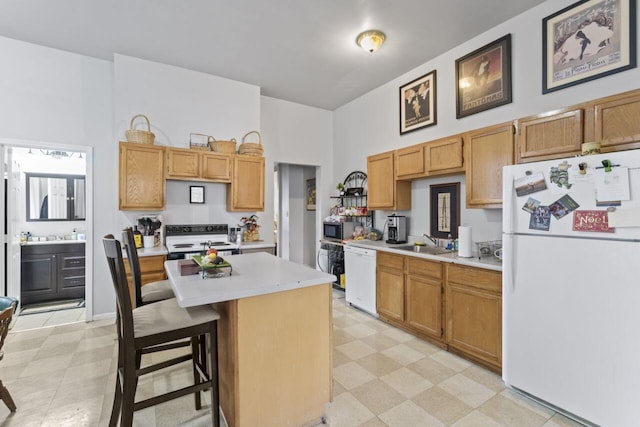 kitchen with a breakfast bar area, sink, white appliances, and light tile floors