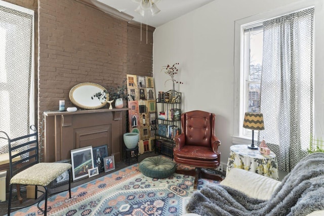 sitting room featuring brick wall, hardwood / wood-style floors, and ceiling fan