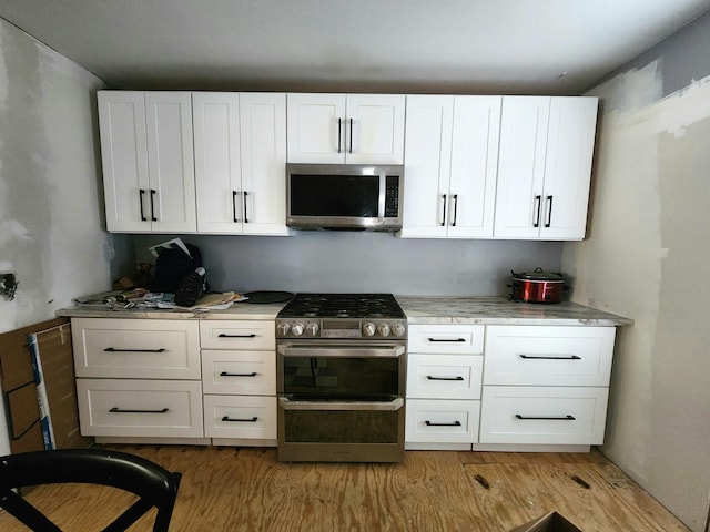 kitchen with appliances with stainless steel finishes, white cabinetry, and light hardwood / wood-style floors