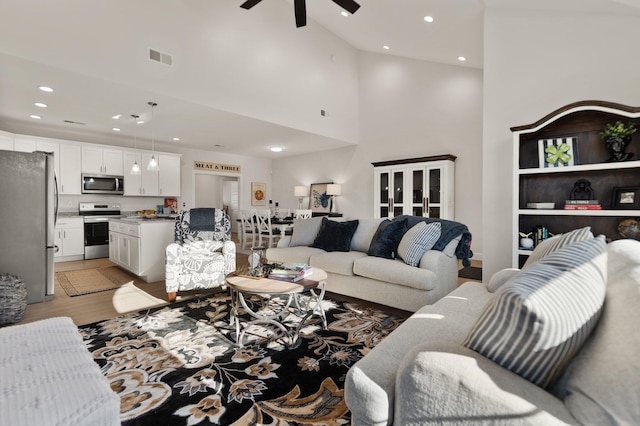 living room with ceiling fan, a high ceiling, and light wood-type flooring