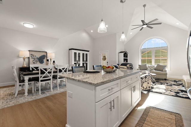 kitchen featuring white cabinetry, light stone counters, dark hardwood / wood-style flooring, a kitchen island, and pendant lighting