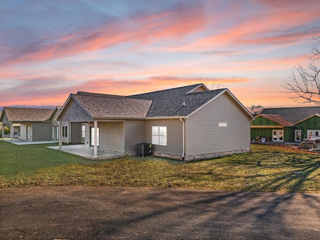 property exterior at dusk with a yard, central AC, and a patio area