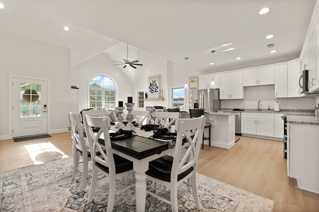 dining area with ceiling fan, sink, high vaulted ceiling, and light wood-type flooring