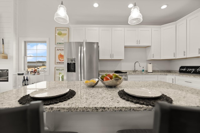 kitchen with hanging light fixtures, white cabinetry, light stone counters, and stainless steel fridge with ice dispenser