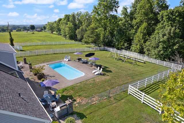 view of swimming pool featuring a rural view, a yard, and a patio area