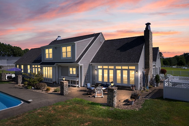 back house at dusk featuring a lawn and a patio area