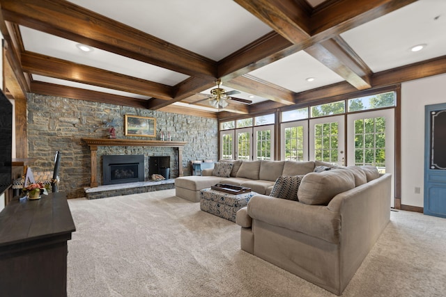 living room featuring light carpet, beamed ceiling, ceiling fan, and a stone fireplace