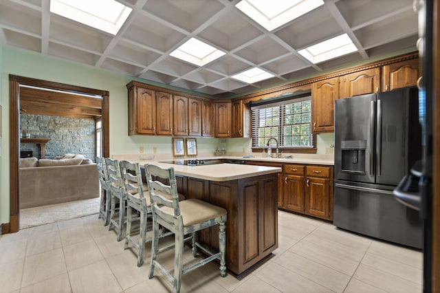 kitchen with stainless steel fridge, coffered ceiling, sink, a kitchen bar, and light tile patterned floors