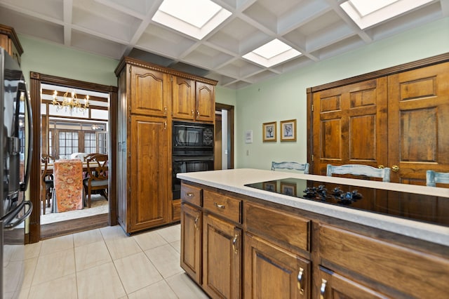 kitchen featuring beamed ceiling, black appliances, a notable chandelier, coffered ceiling, and light tile patterned floors