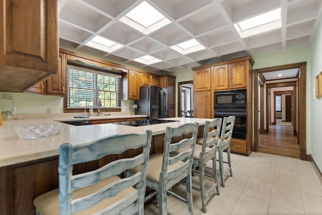 kitchen featuring coffered ceiling, a breakfast bar area, light tile patterned flooring, and black appliances