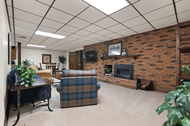 carpeted living room with a drop ceiling, a brick fireplace, and brick wall