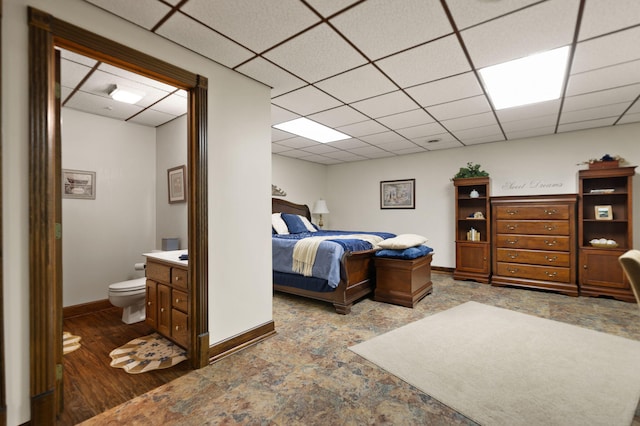 bedroom with a paneled ceiling, hardwood / wood-style flooring, and ensuite bath