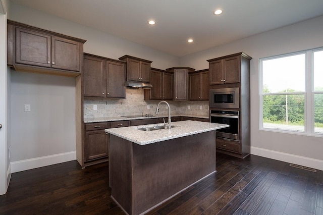 kitchen featuring an island with sink, stainless steel appliances, backsplash, dark hardwood / wood-style flooring, and sink