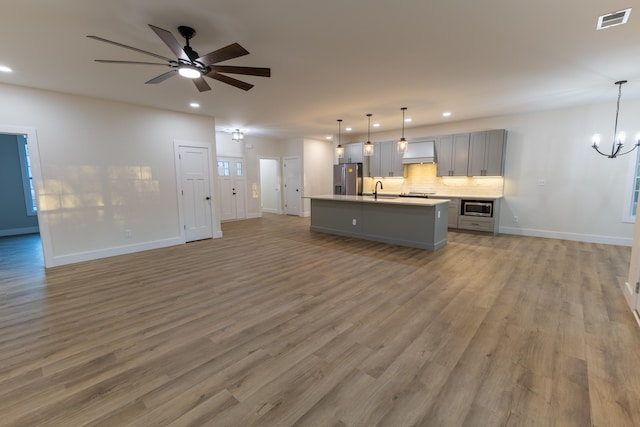 unfurnished living room with hardwood / wood-style flooring, ceiling fan with notable chandelier, and sink