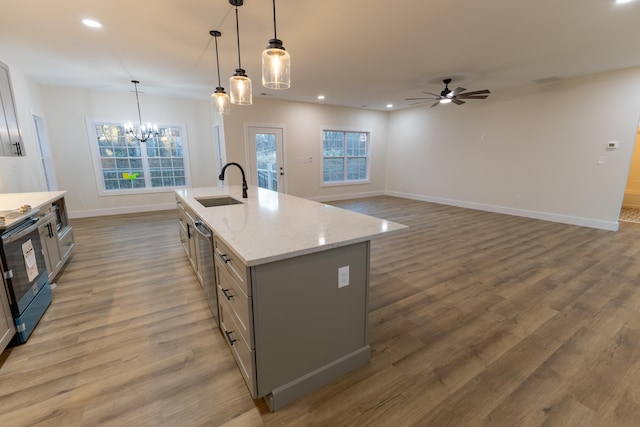 kitchen with stainless steel appliances, a center island with sink, sink, decorative light fixtures, and light hardwood / wood-style flooring