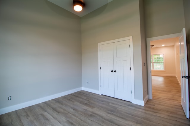 unfurnished bedroom featuring a towering ceiling, light wood-type flooring, ceiling fan, and a closet