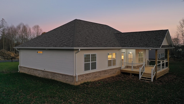 back house at dusk with a deck and a lawn