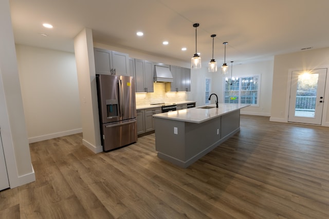 kitchen featuring gray cabinetry, stainless steel fridge, pendant lighting, an island with sink, and custom exhaust hood