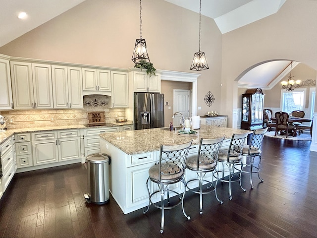 kitchen featuring a breakfast bar, hanging light fixtures, a kitchen island with sink, stainless steel fridge with ice dispenser, and light stone countertops