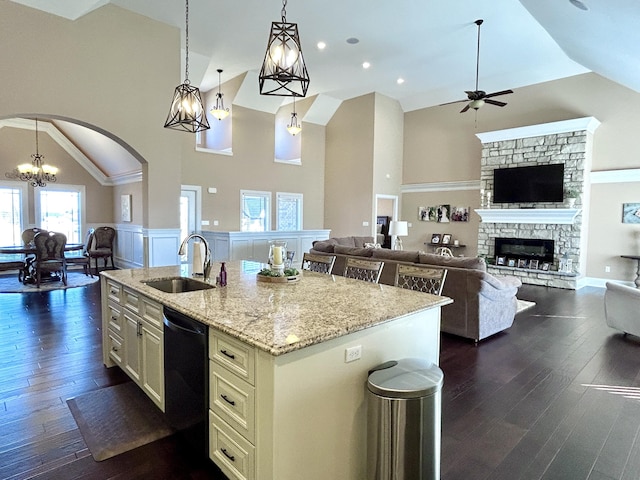 kitchen with sink, a kitchen island with sink, black dishwasher, light stone counters, and decorative light fixtures