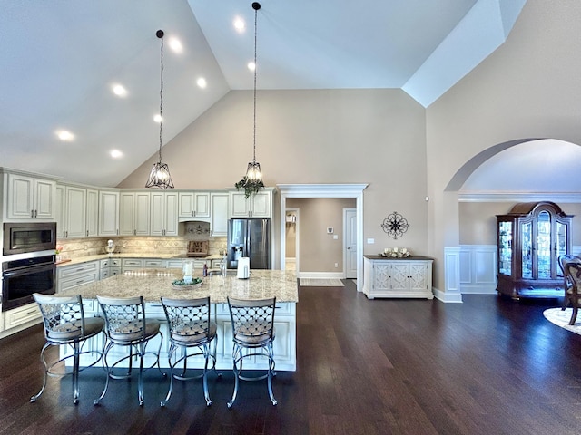 kitchen with a spacious island, appliances with stainless steel finishes, decorative light fixtures, and light stone counters