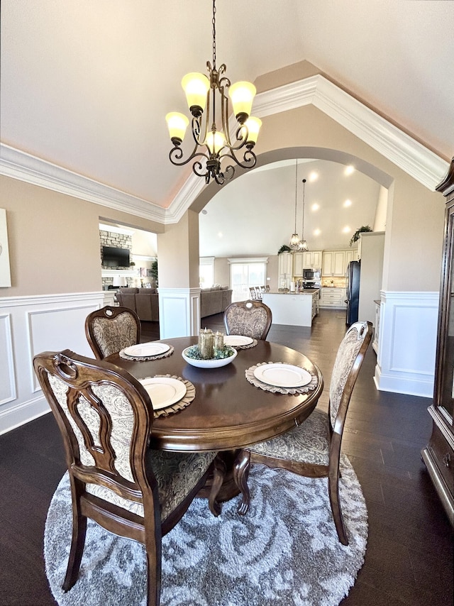 dining area featuring lofted ceiling, a notable chandelier, crown molding, and dark wood-type flooring