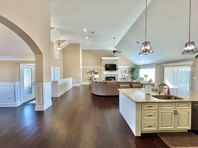 kitchen with a stone fireplace, decorative light fixtures, sink, light stone counters, and dark wood-type flooring