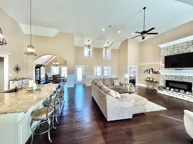 living room featuring a stone fireplace, sink, high vaulted ceiling, and dark hardwood / wood-style flooring