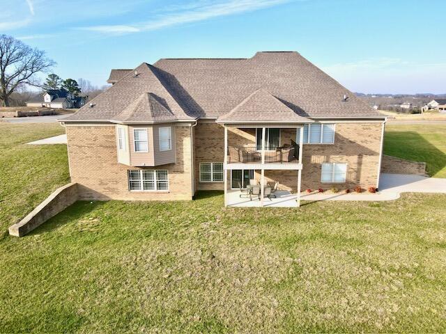 rear view of house featuring a balcony, a patio, and a lawn