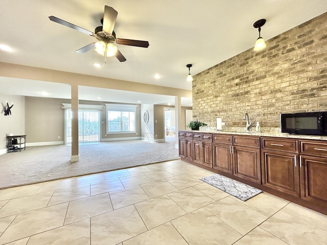 kitchen featuring sink, decorative light fixtures, light colored carpet, brick wall, and light stone countertops