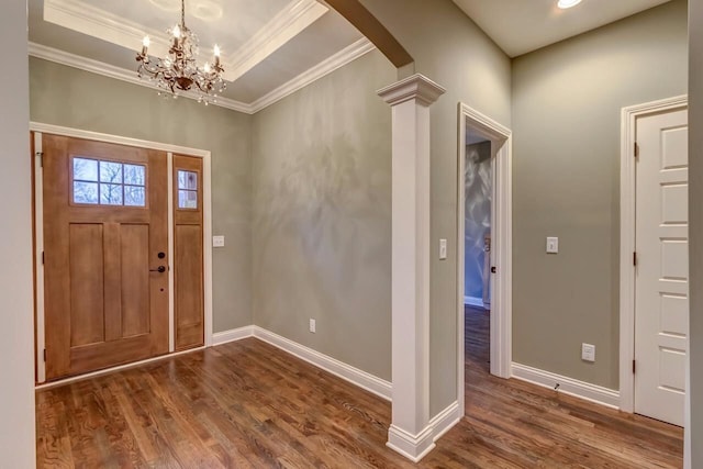 foyer featuring a notable chandelier, ornamental molding, dark wood-type flooring, a raised ceiling, and decorative columns