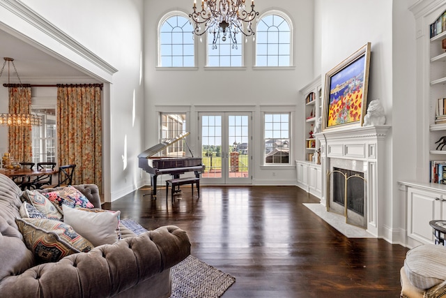 living room featuring a high end fireplace, dark hardwood / wood-style flooring, built in shelves, a chandelier, and a towering ceiling