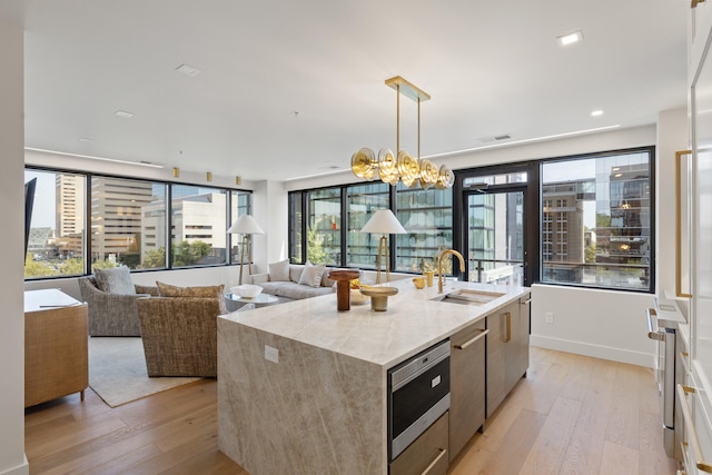 kitchen with light wood-type flooring, sink, an island with sink, and hanging light fixtures