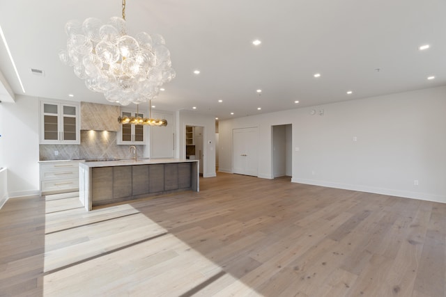 kitchen with a spacious island, tasteful backsplash, sink, and light hardwood / wood-style floors