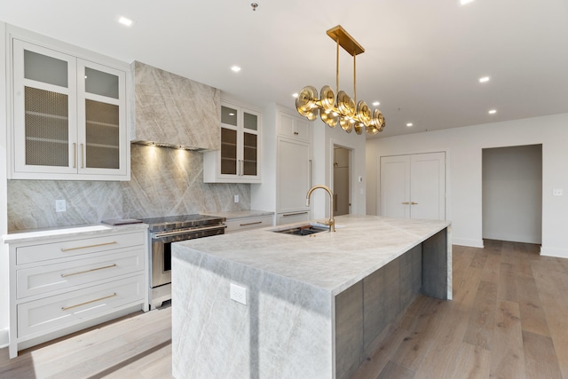 kitchen with a large island with sink, light hardwood / wood-style flooring, sink, white cabinets, and electric stove