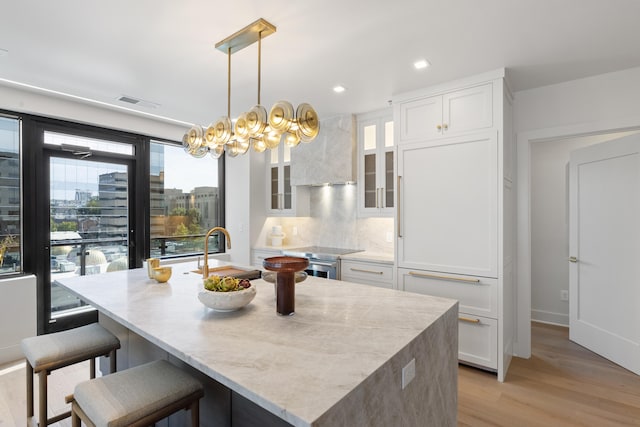 kitchen featuring an island with sink, white cabinetry, light wood-type flooring, and pendant lighting