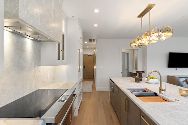 kitchen featuring wall chimney exhaust hood, sink, pendant lighting, light stone counters, and light hardwood / wood-style floors