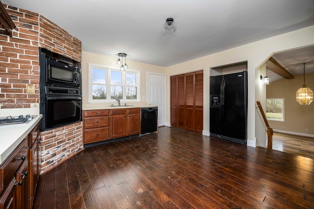 kitchen with an inviting chandelier, dark wood-type flooring, black appliances, hanging light fixtures, and sink