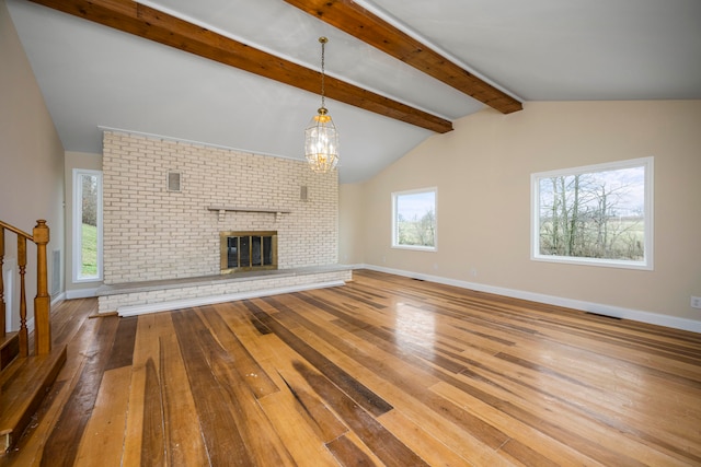 unfurnished living room with a notable chandelier, brick wall, a brick fireplace, and light hardwood / wood-style floors