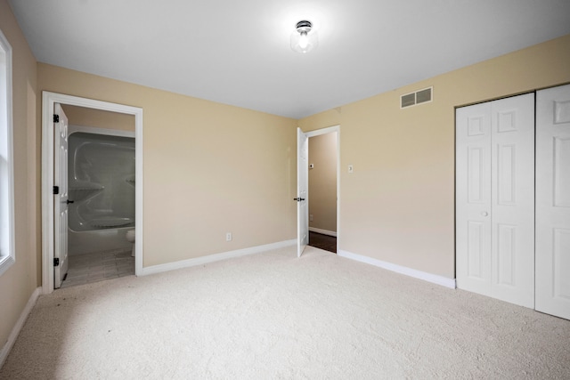 unfurnished bedroom with light carpet, ensuite bath, and a closet